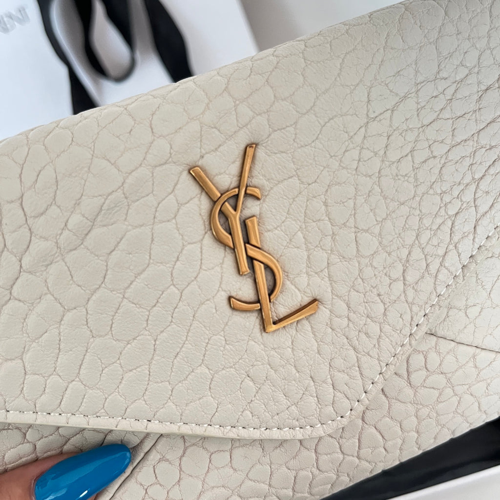 Close-up of light off-white textured flap with gold-tone YSL logo and stitched edge