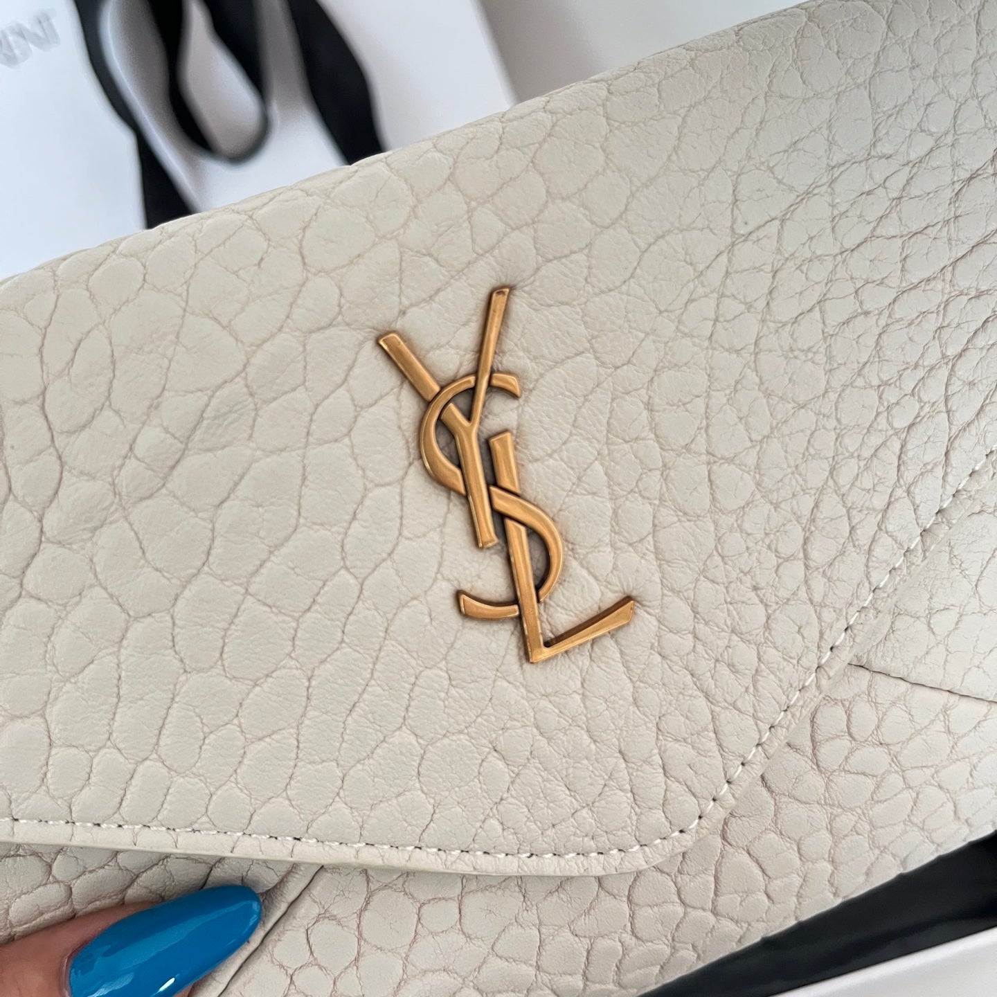 Close-up of light off-white textured flap with gold-tone YSL logo and stitched edge