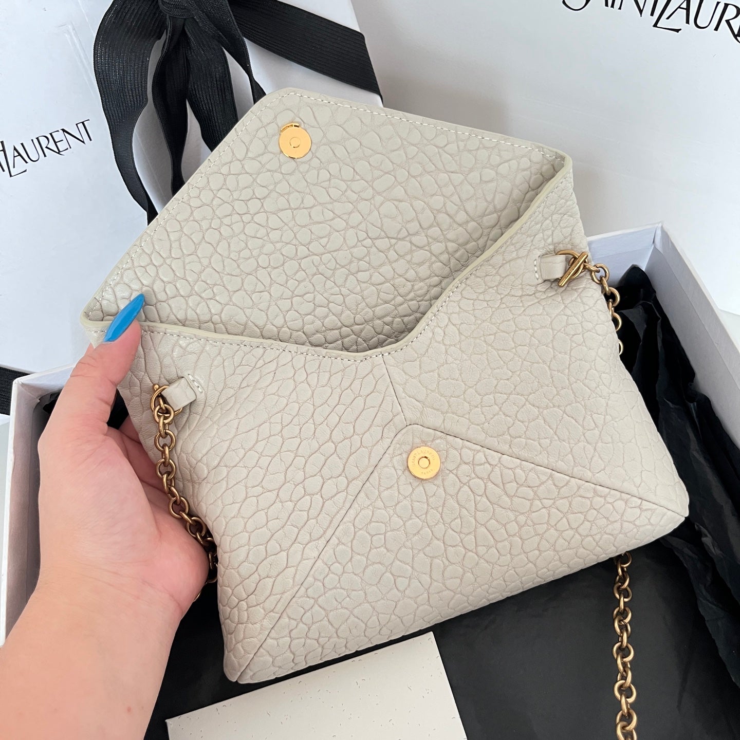 Light off-white textured shoulder bag with front flap, gold button accents, and chain strap