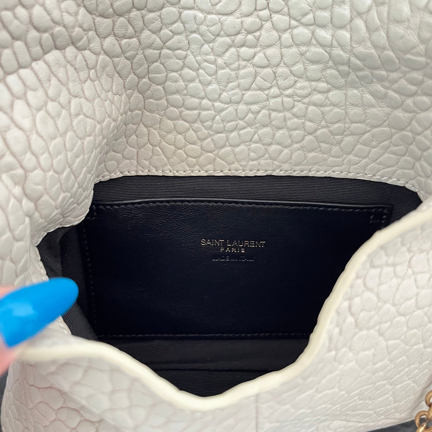 Close-up of light off-white textured flap interior lining with small Saint Laurent label