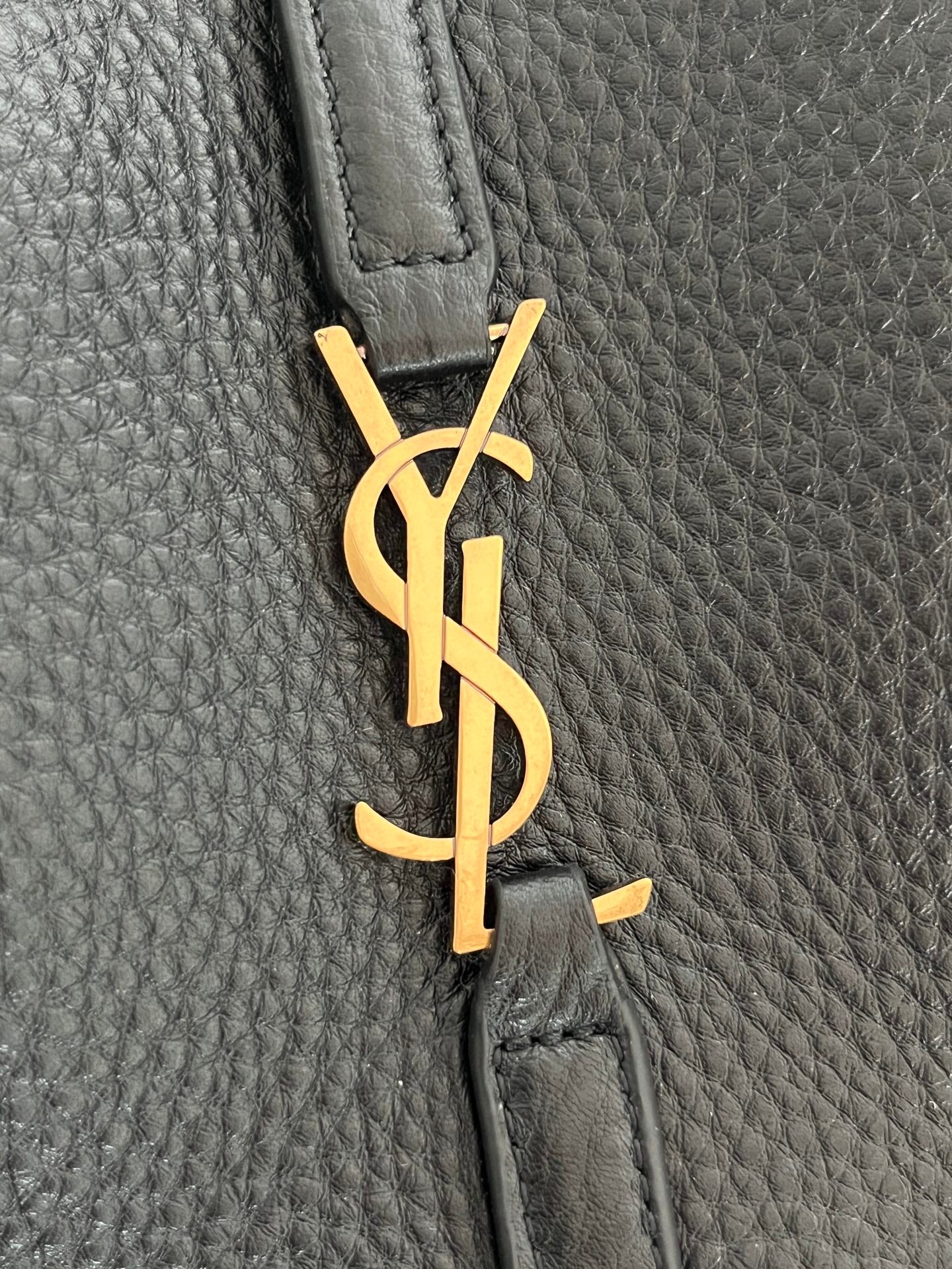 YSL bag detail, gold monogram charm on black pebbled leather