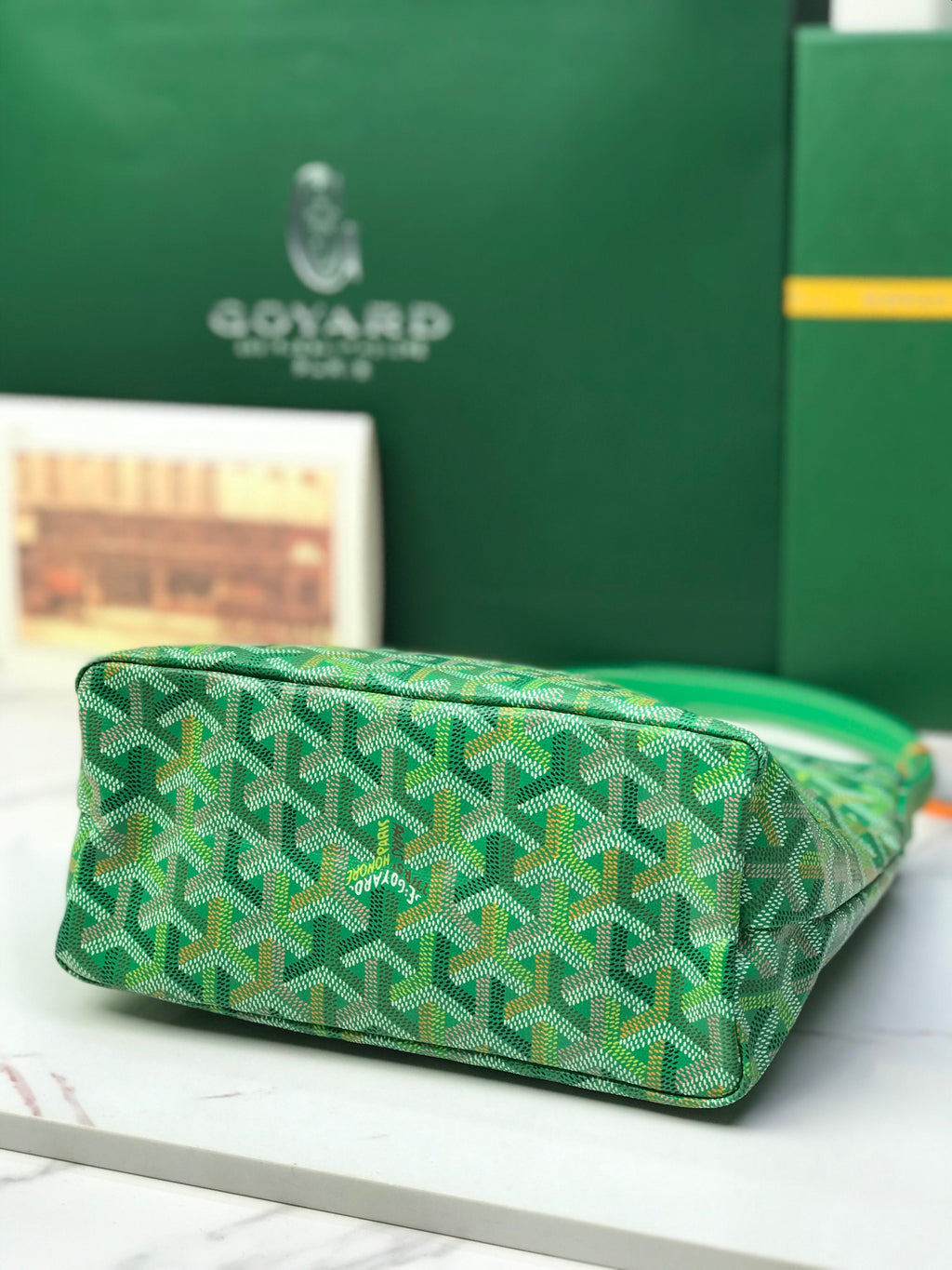Green Goyard patterned tote bag laid down, showing textured base and top edge.