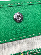 Green leather Goyard bag front with round metal logo stud and contrast stitching.