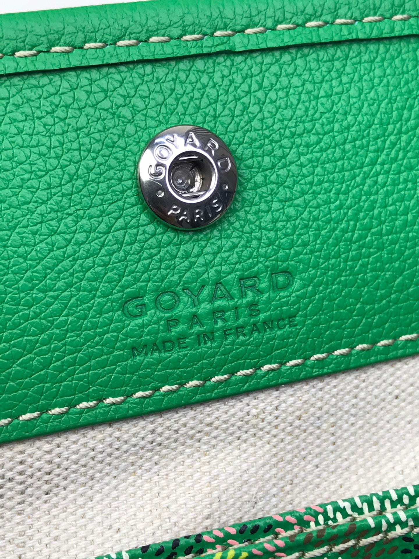 Green leather Goyard bag front with round metal logo stud and contrast stitching.