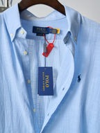 Light blue polo shirt with button placket, collar tag, and navy pony logo