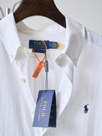 White button-up shirt with navy polo logo and yellow buttons; hanging tags