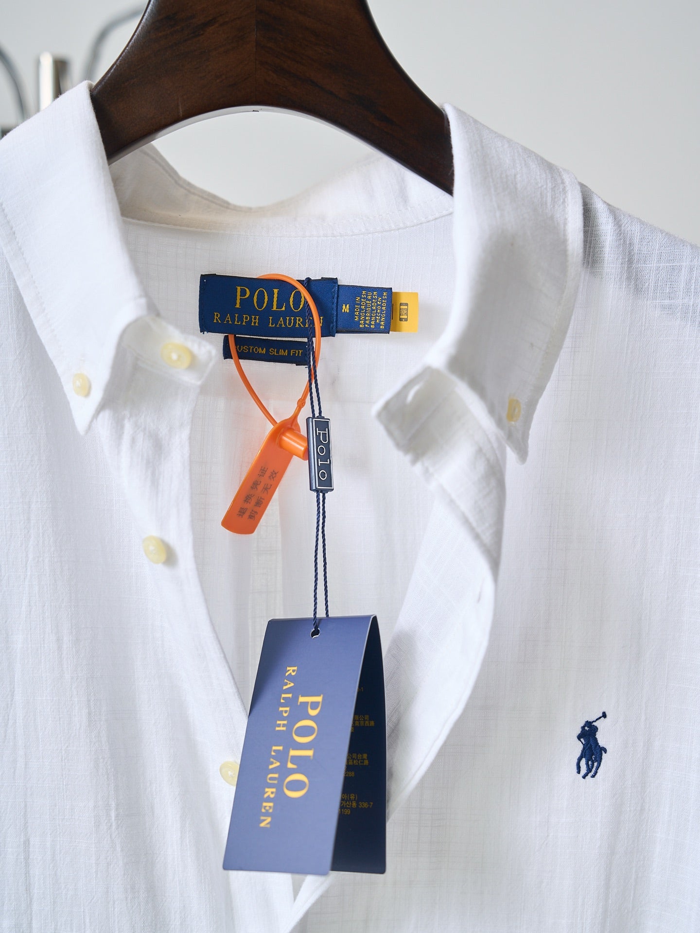 White button-up shirt with navy polo logo and yellow buttons; hanging tags