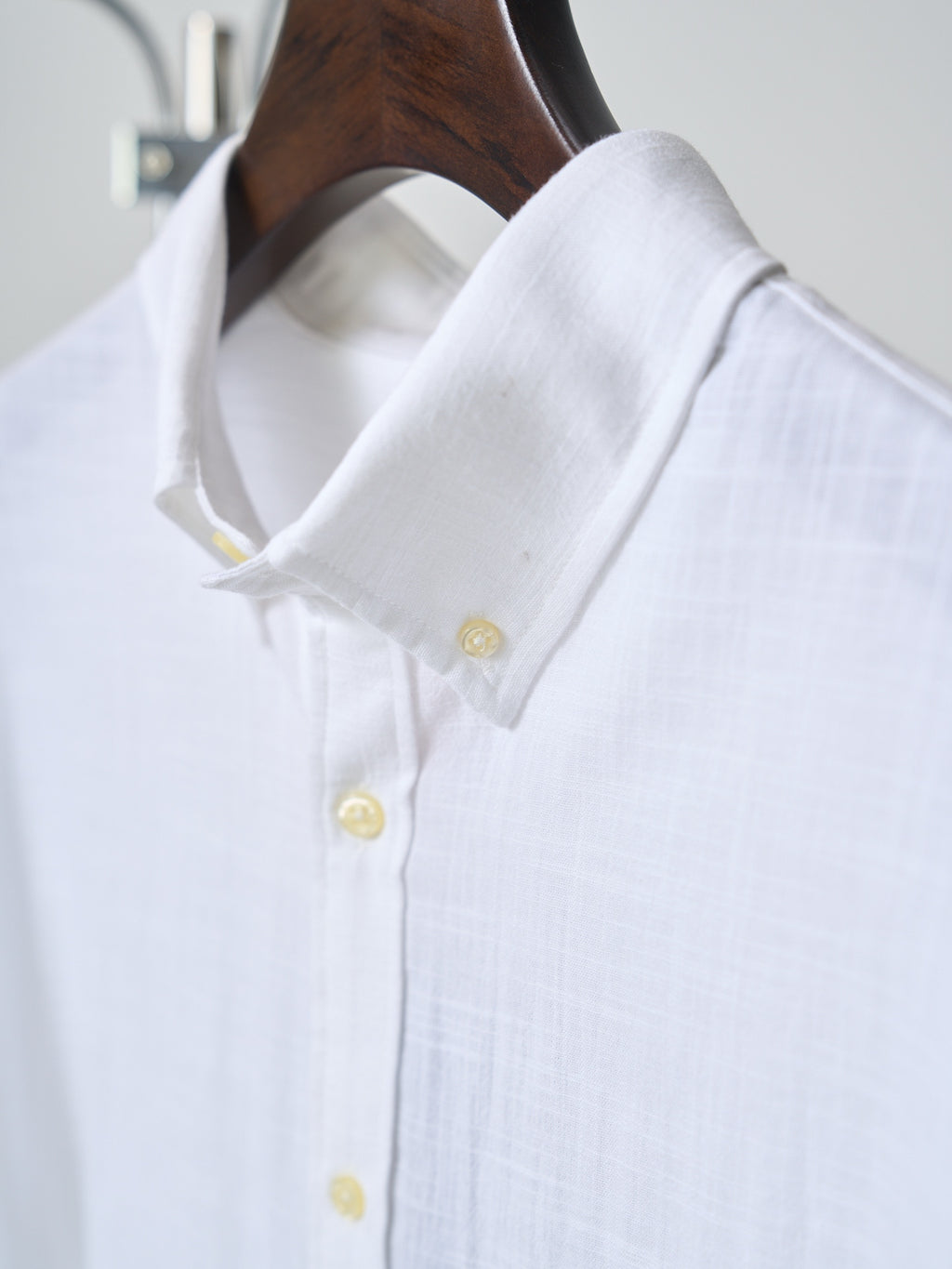 White button-up shirt collar with yellow buttons and small gold logo detail