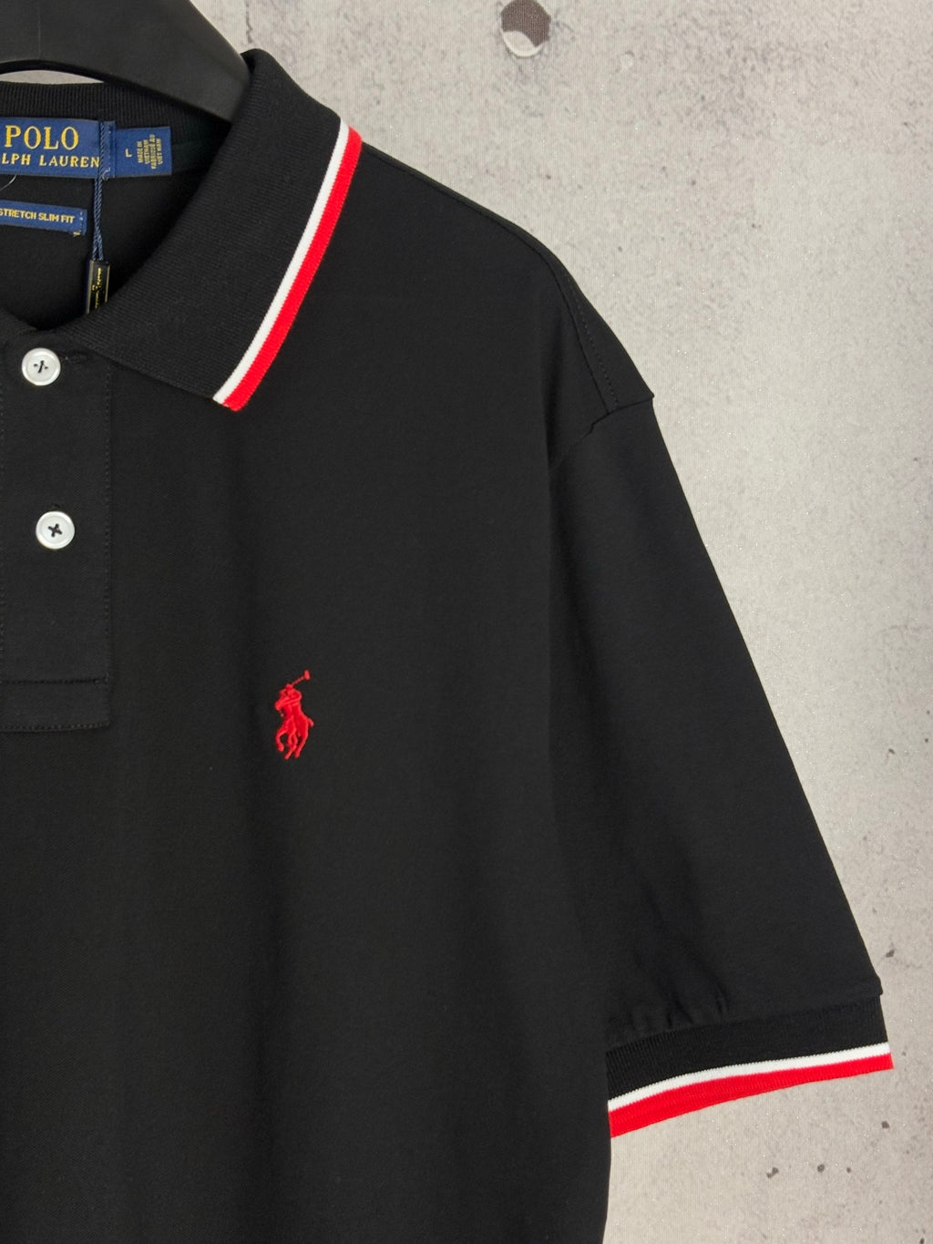 Black polo shirt sleeve with red pony logo and red/white hem stripe