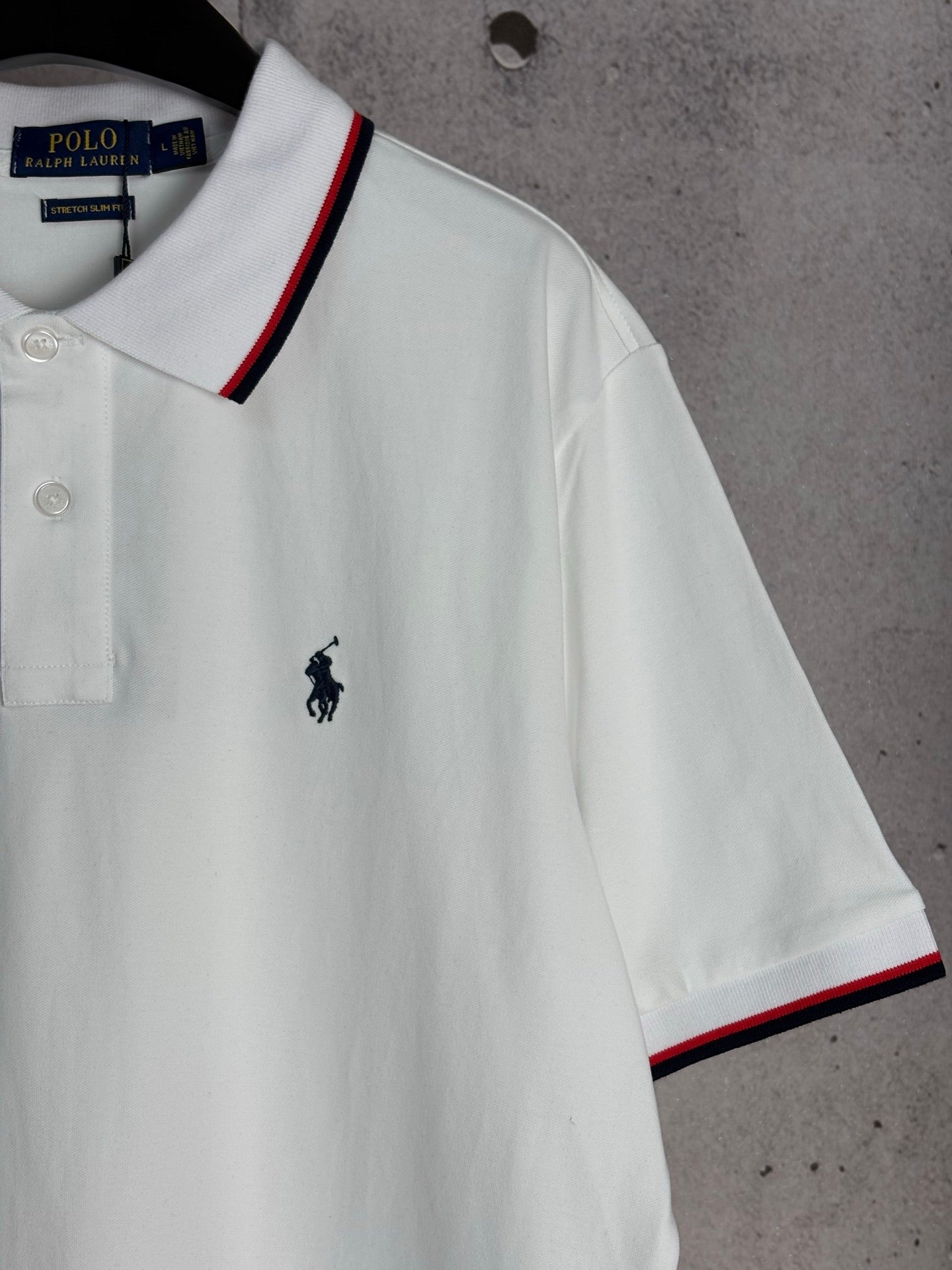 White polo shirt with embroidered horse logo and red-and-navy trim at sleeve hem