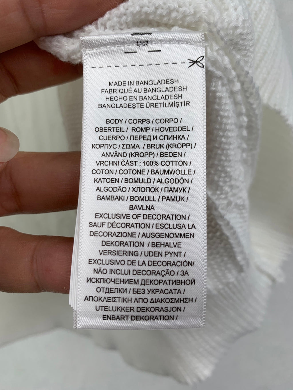 Clothing care tag on white knit polo shirt; 100% cotton and made in Bangladesh
