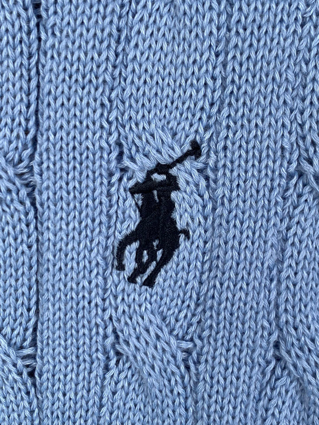 Close-up of light blue cable knit texture with black horse logo patch