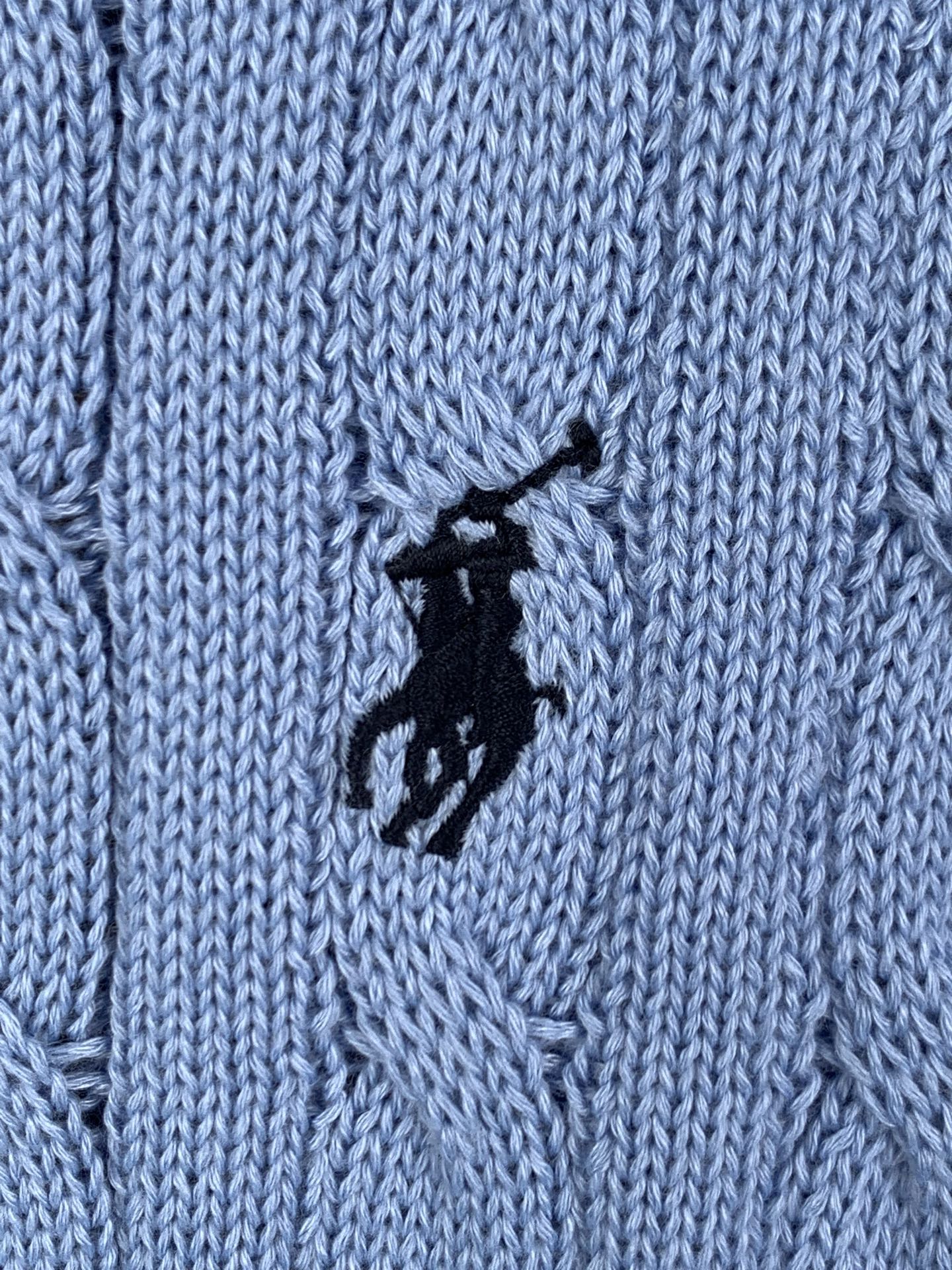 Close-up of light blue cable knit texture with black horse logo patch