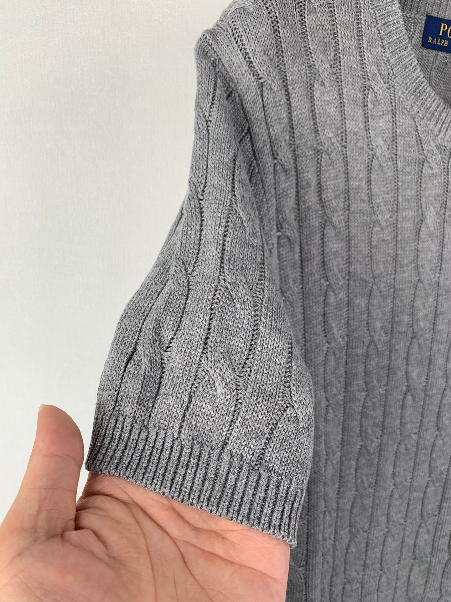 Gray knit polo sleeve with ribbed cuff and cable texture, shown in close-up