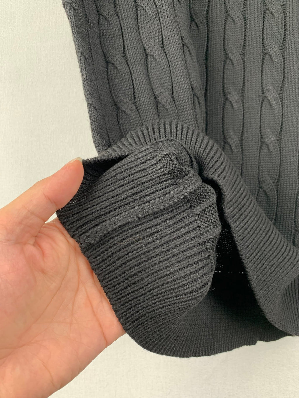 Ribbed sleeve cuff detail on dark cable-knit sweater fabric