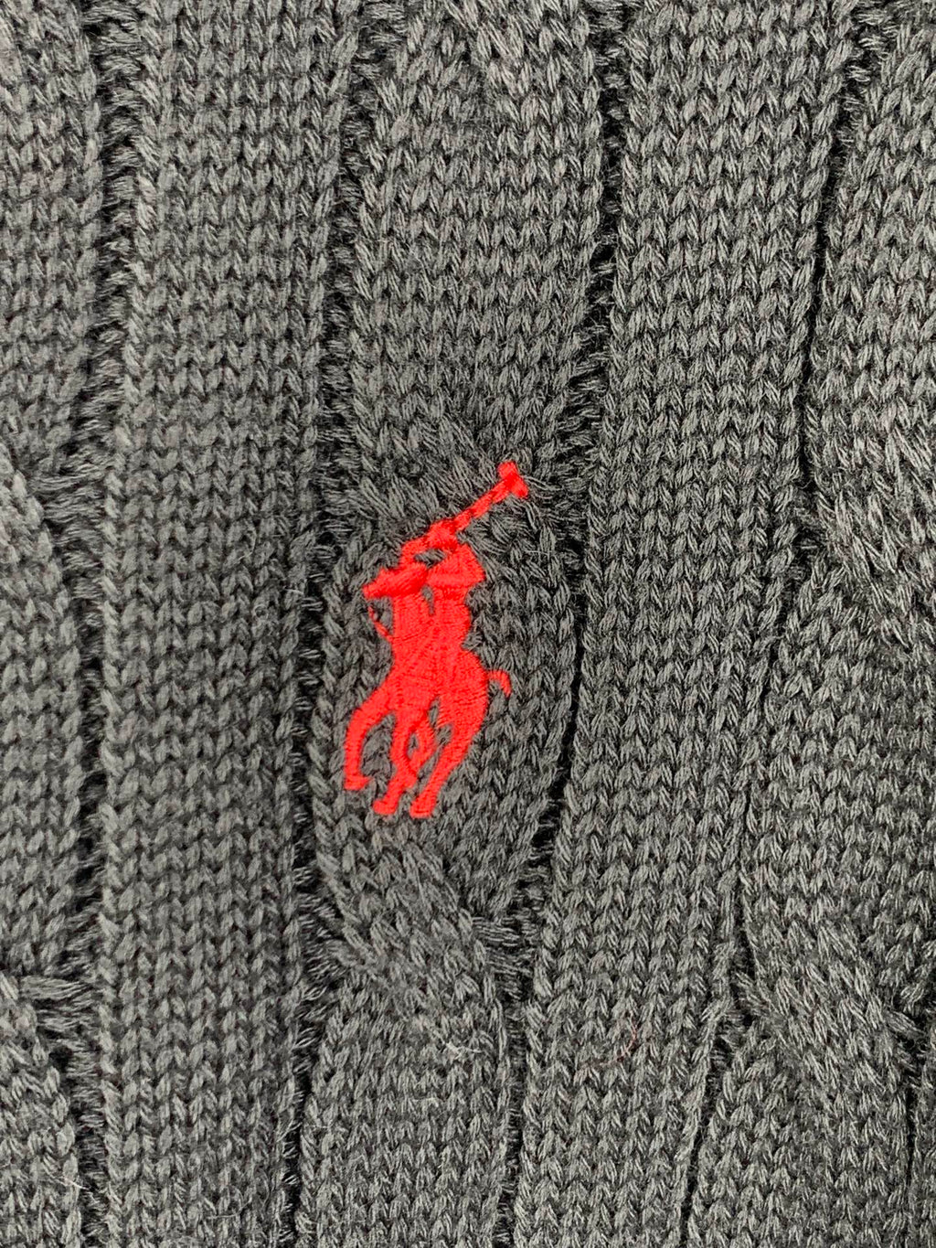 Red polo player logo on dark cable-knit sweater fabric