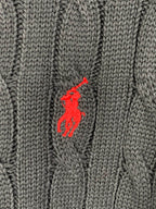 Red polo player logo on dark cable-knit sweater fabric