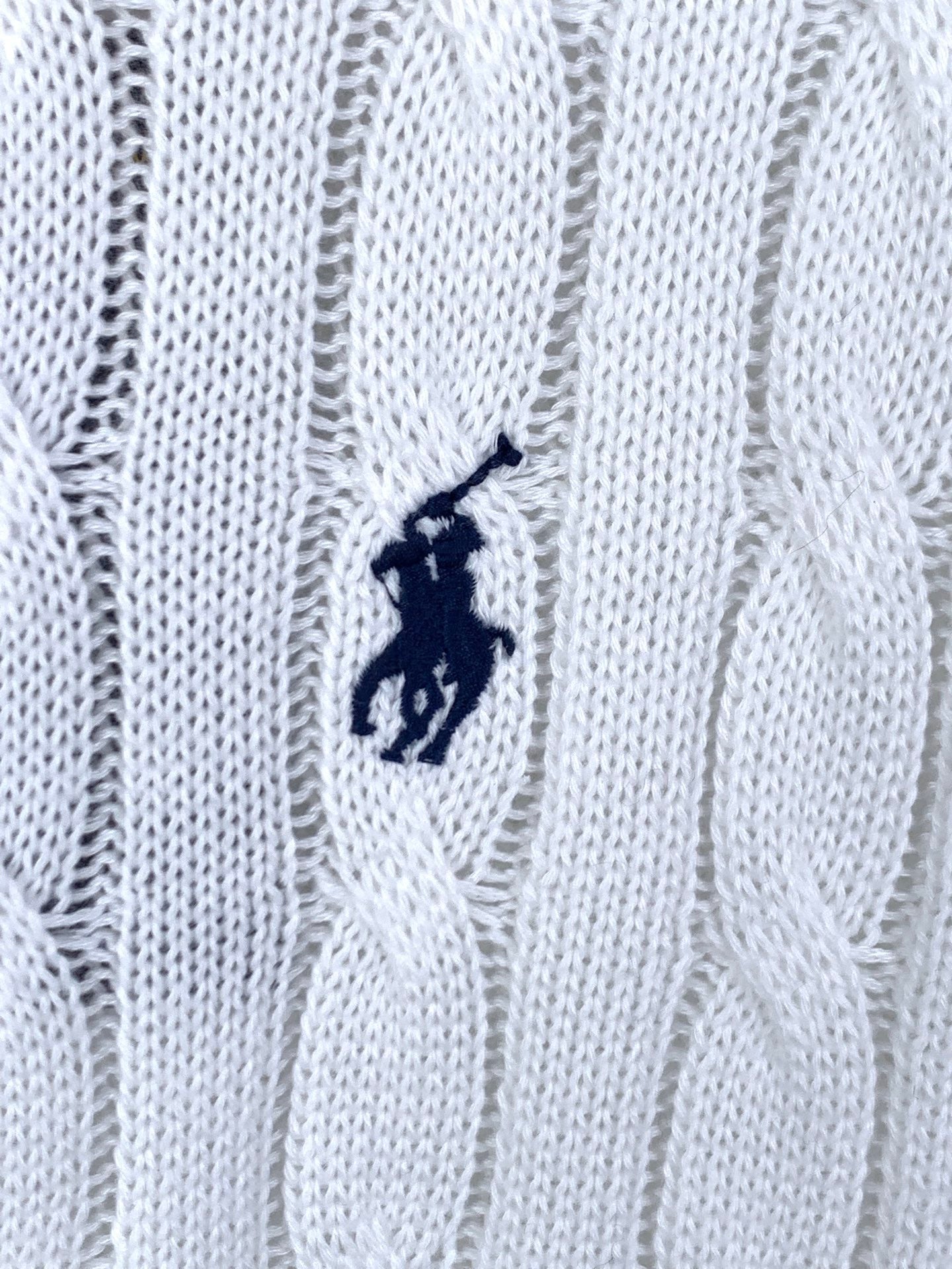 Small navy polo logo embroidered on white cable-knit sweater fabric