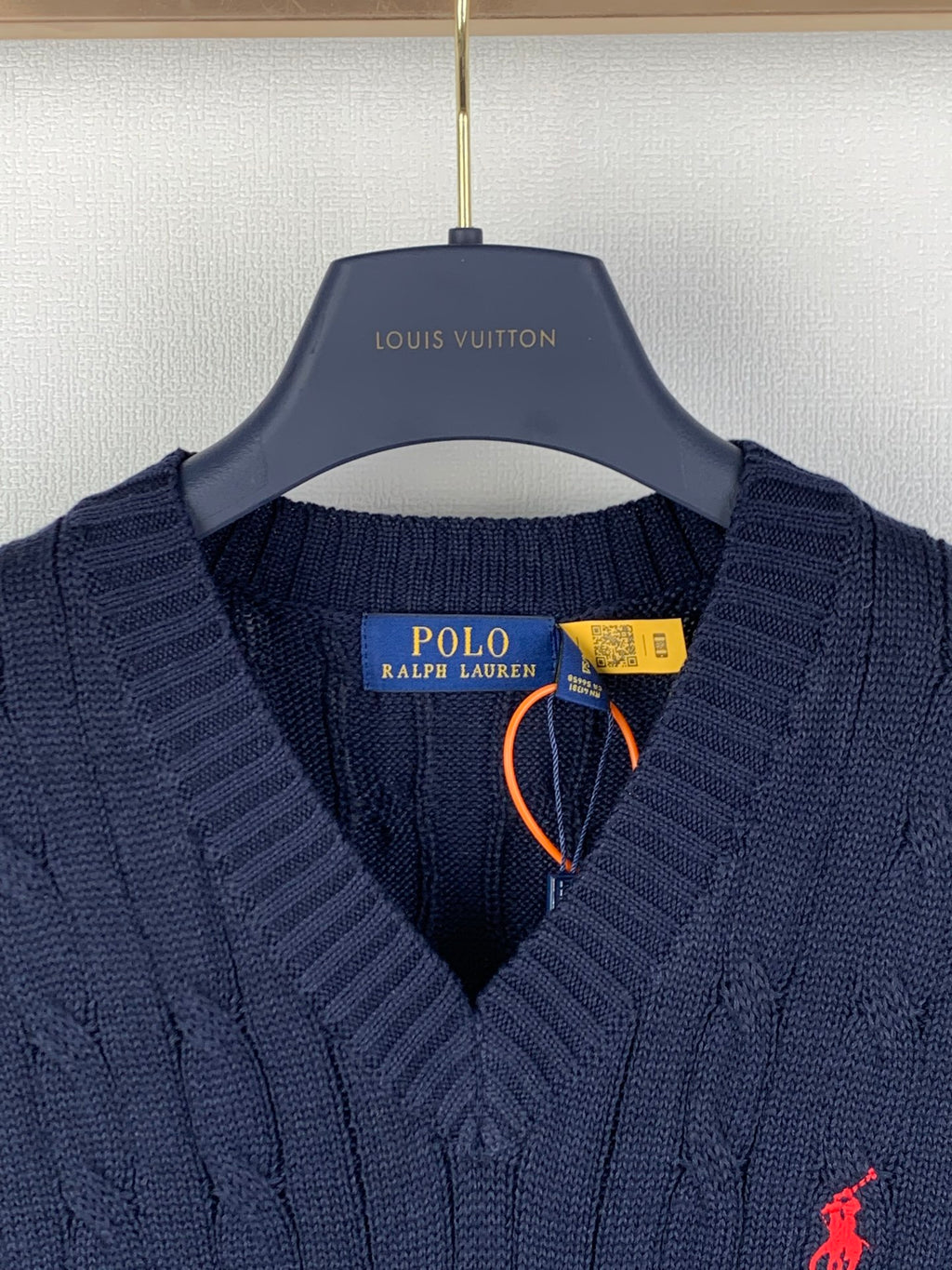 Navy cable-knit sweater vest with V-neck, red polo logo, and neck tag