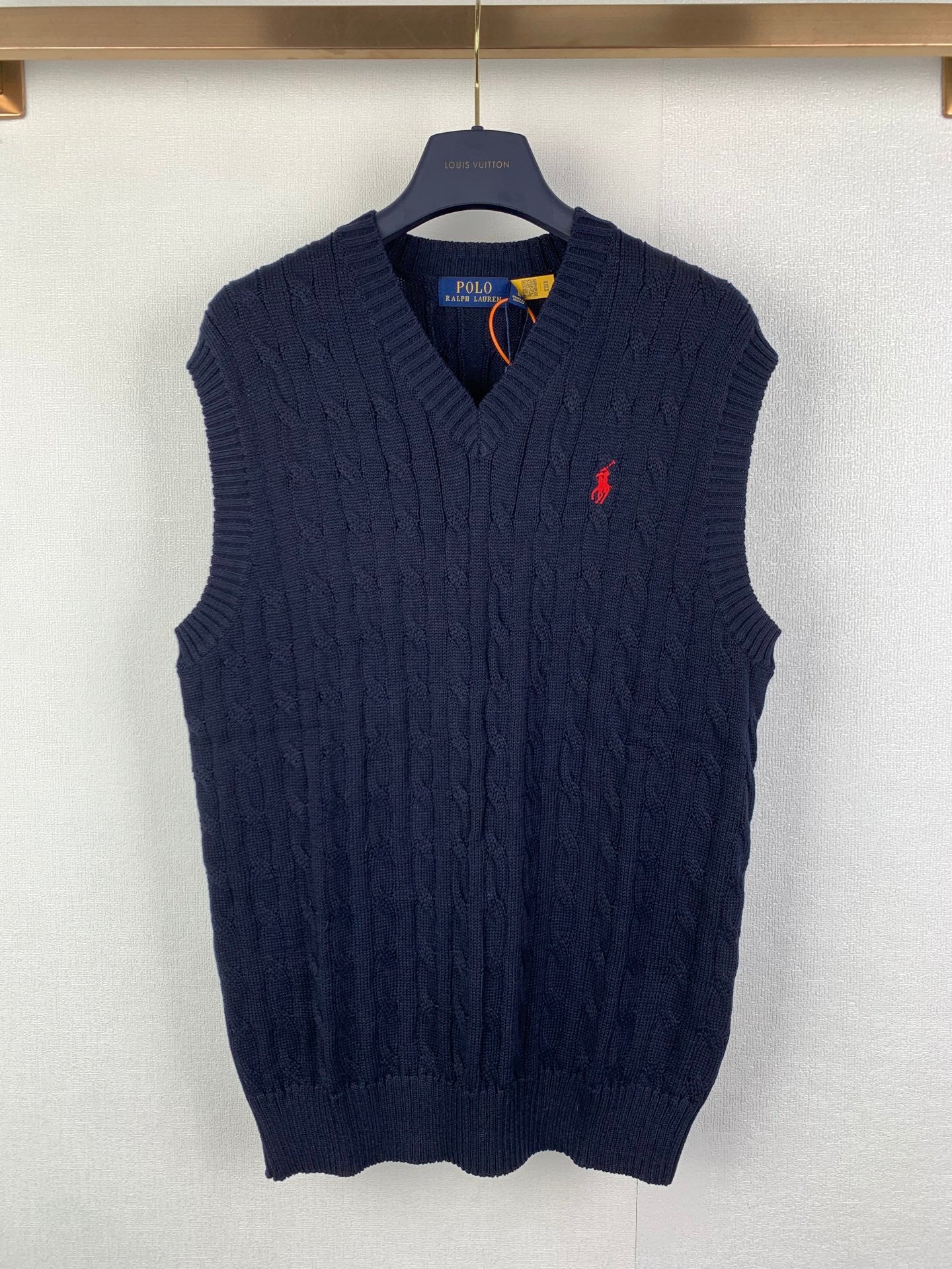 Navy cable-knit sweater vest with V-neck and small red logo on chest