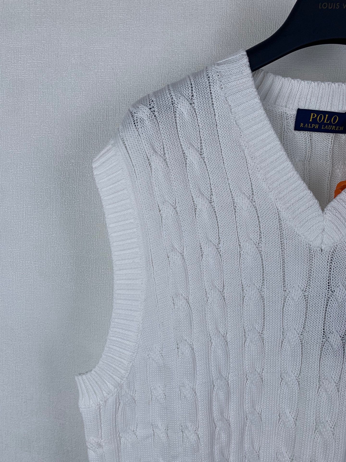 White cable-knit sweater vest detail with V-neck ribbed trim