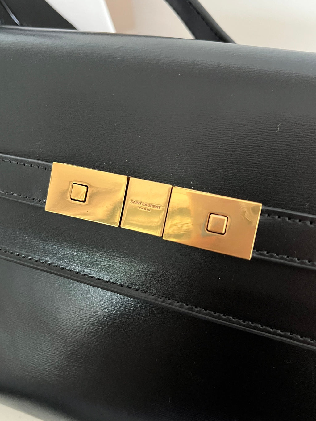 Black YSL handbag front flap with rectangular gold-tone lock plates