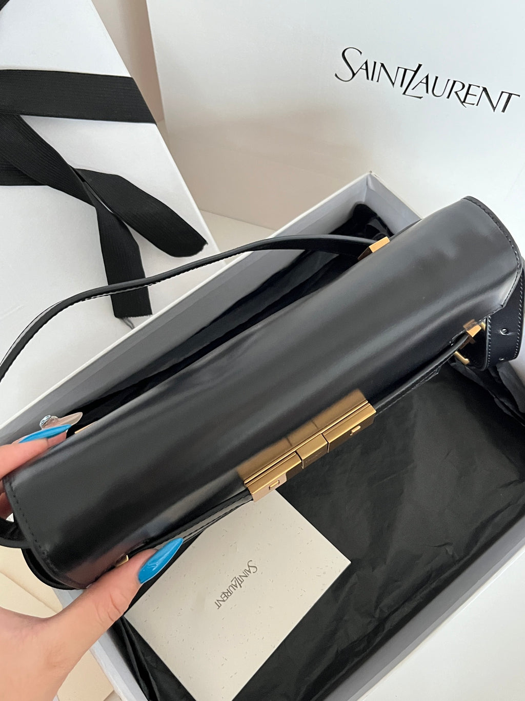 Black YSL handbag laid flat with gold-tone clasp and long strap