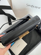 Black YSL handbag laid flat with gold-tone clasp and long strap