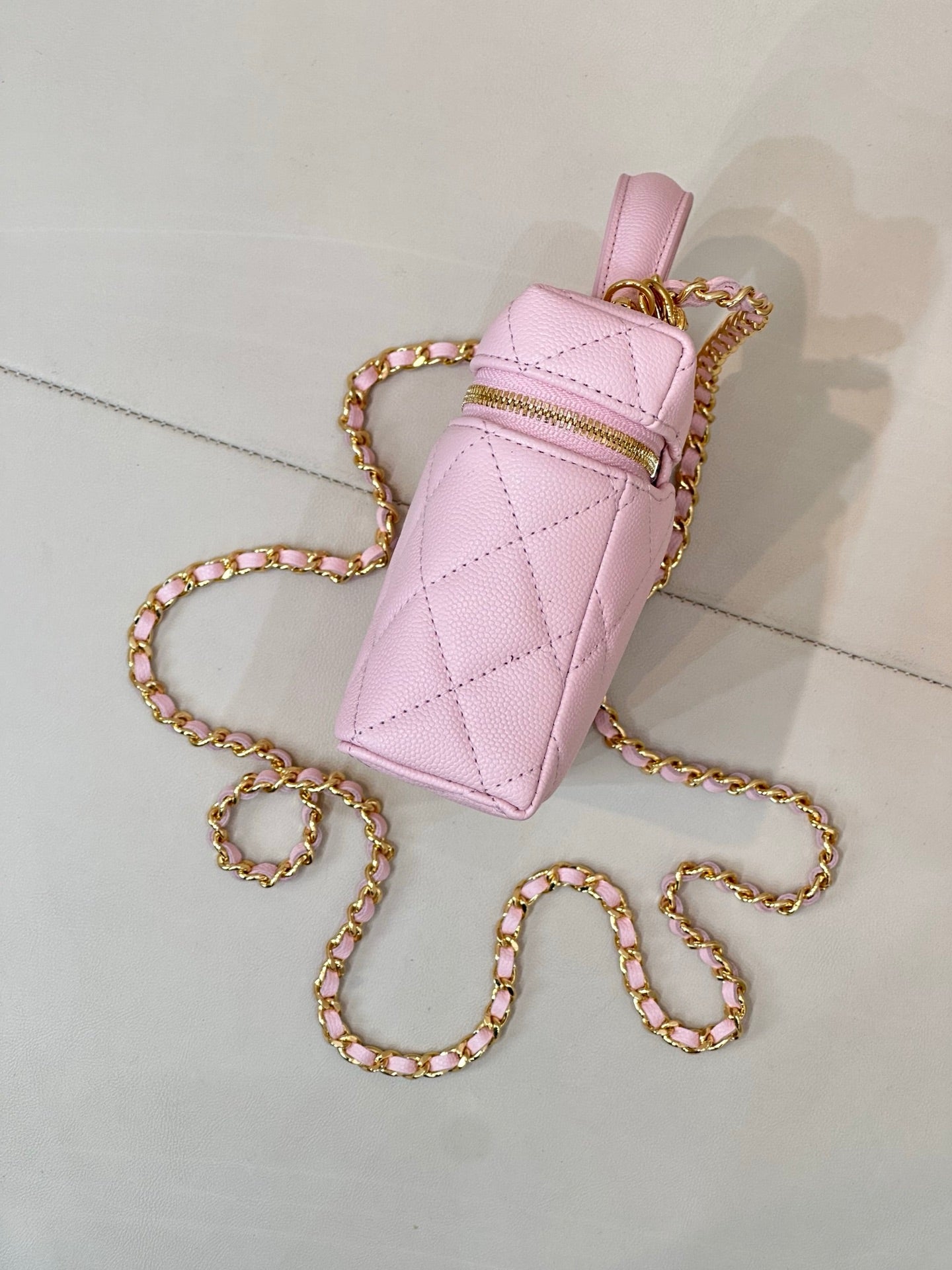Pink quilted mini bag with top handle, gold logo charm, and jeweled chain crossbody strap