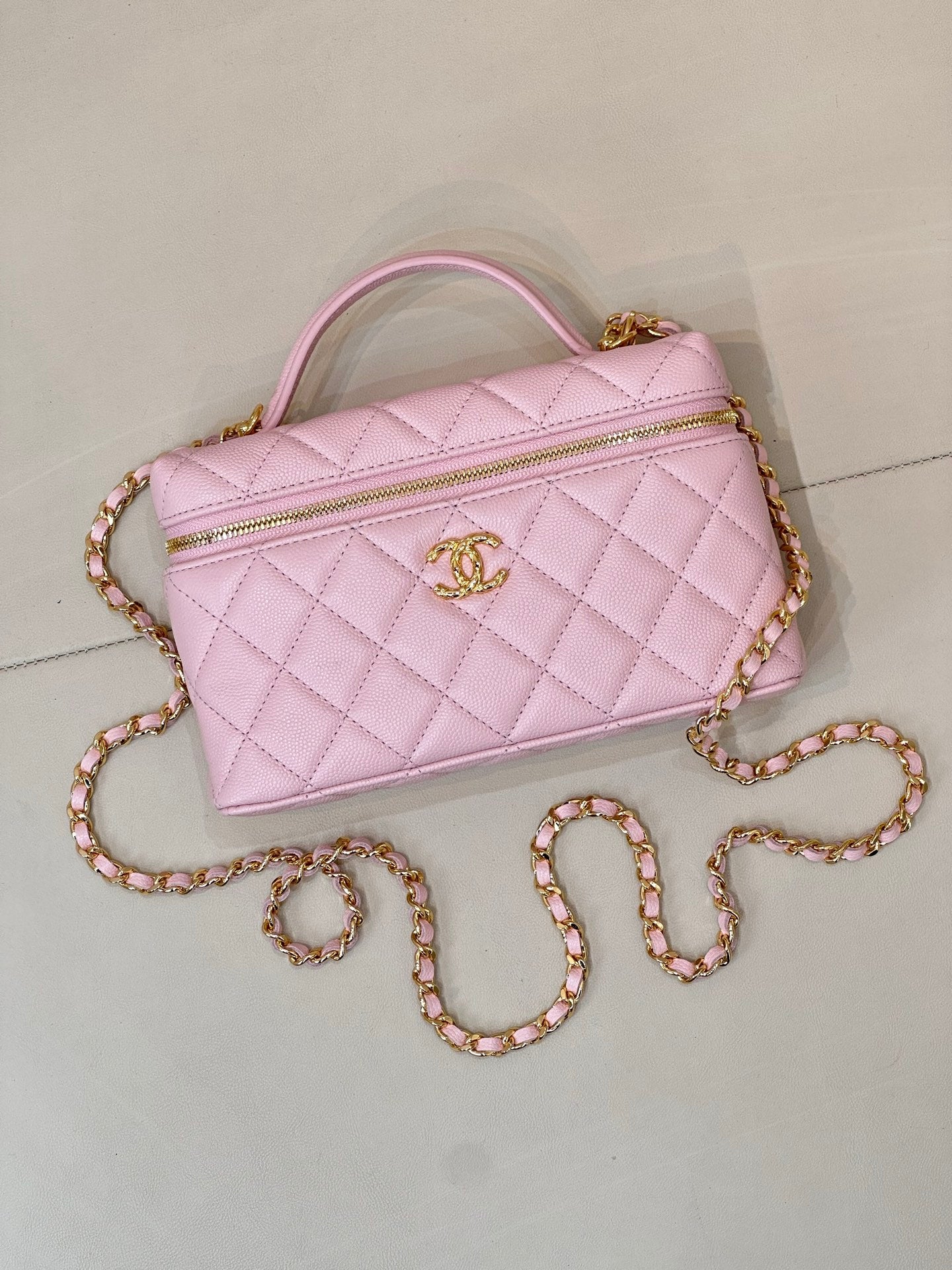 Pink quilted mini handbag with top handle, gold logo charm, and long jeweled chain strap