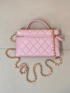 Pink quilted handbag with top handle, gold logo charm, zipper, and jeweled chain strap