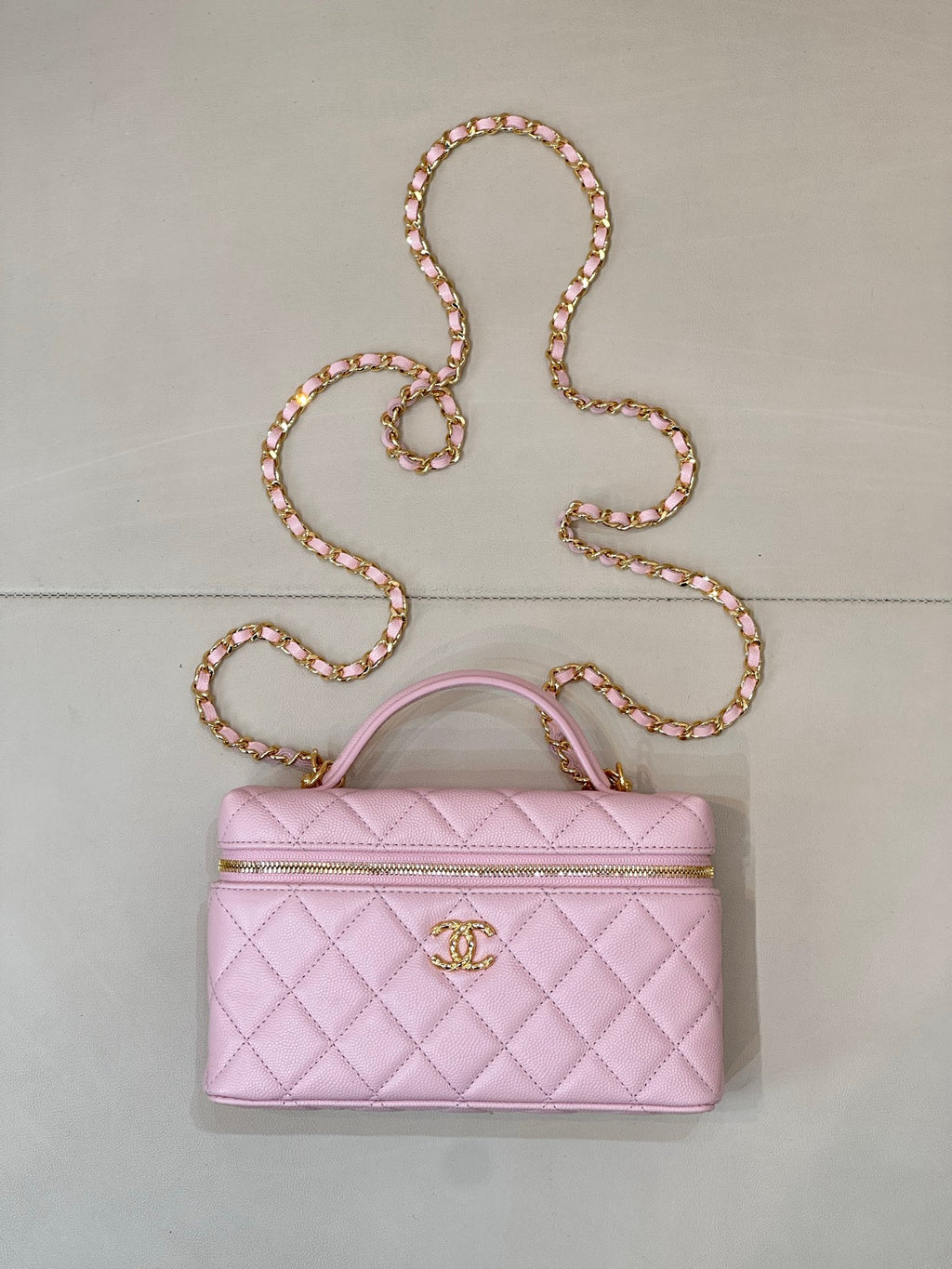 Pink quilted handbag with top handle, gold logo charm, and long jeweled chain strap