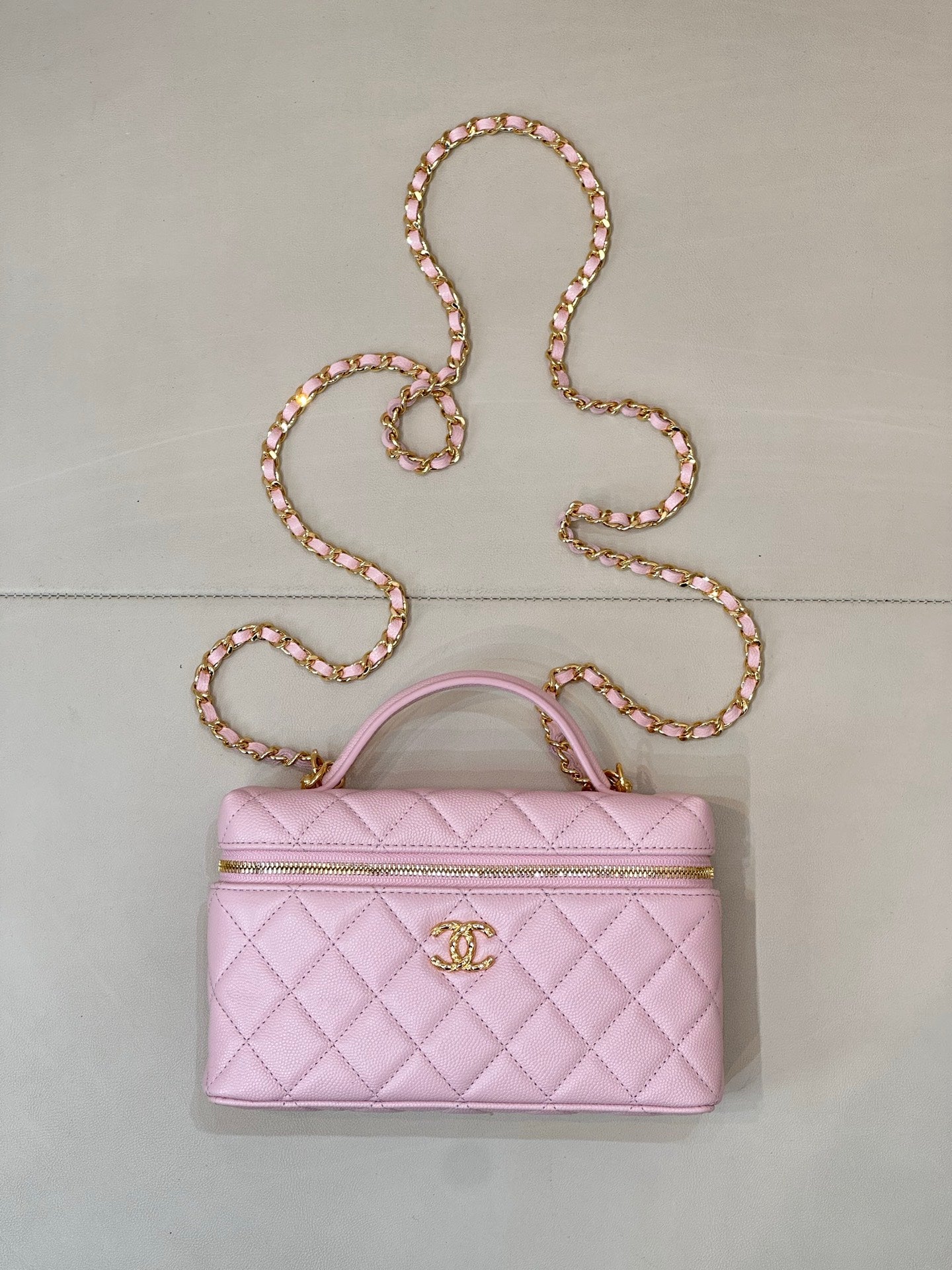 Pink quilted handbag with top handle, gold logo charm, and long jeweled chain strap