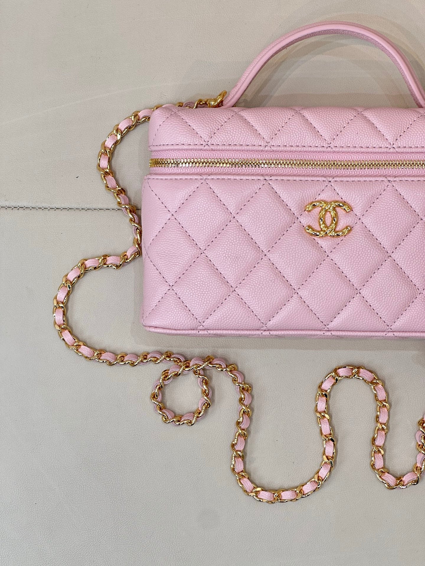 Pink quilted handbag with top zipper, gold logo charm, and jeweled crossbody chain strap
