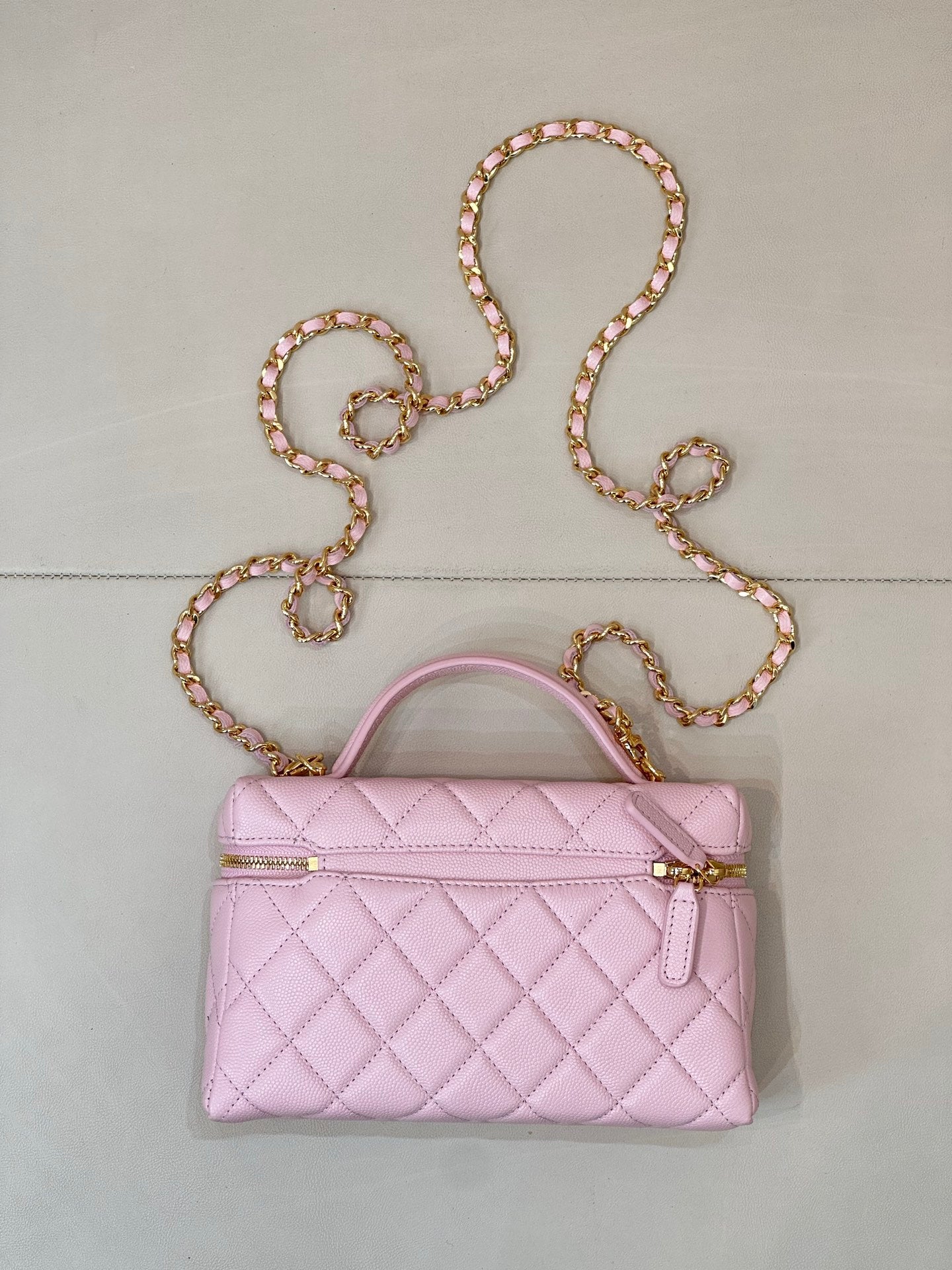 Pink quilted handbag with top handle, gold logo charm, and jeweled chain strap