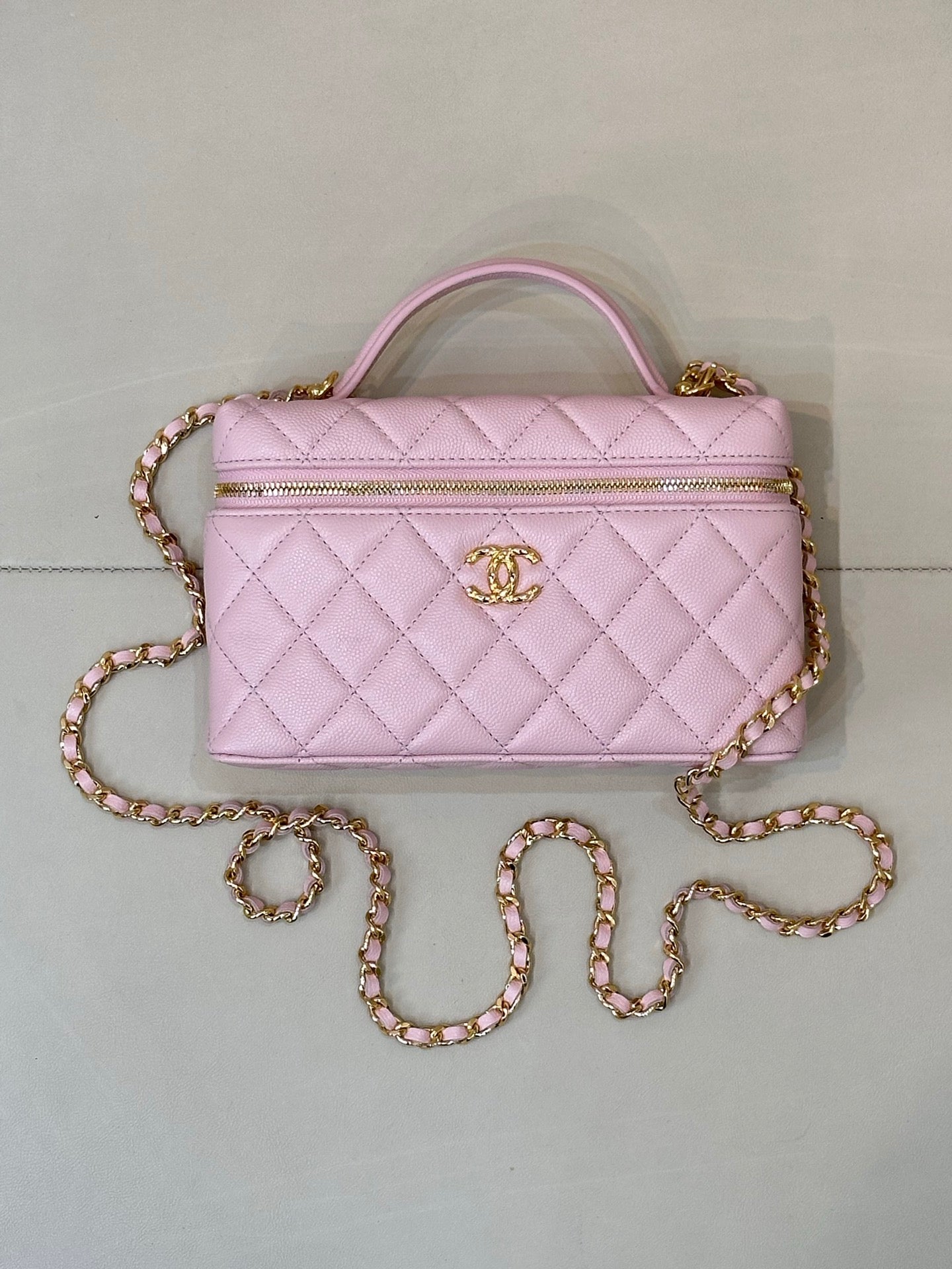 Pink quilted Chanel-style handbag with top handle, zipper top, and jeweled chain strap