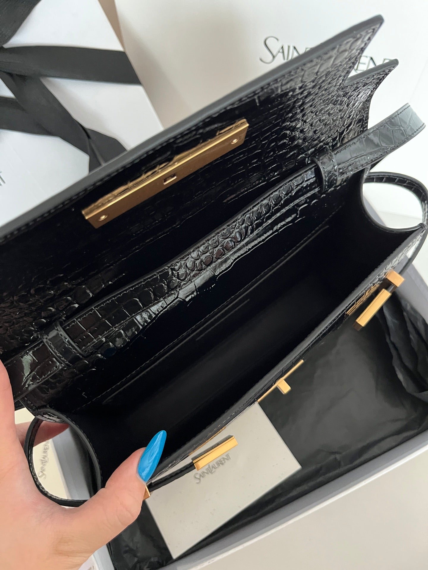Black crocodile-embossed handbag interior view with gold bar hardware and strap
