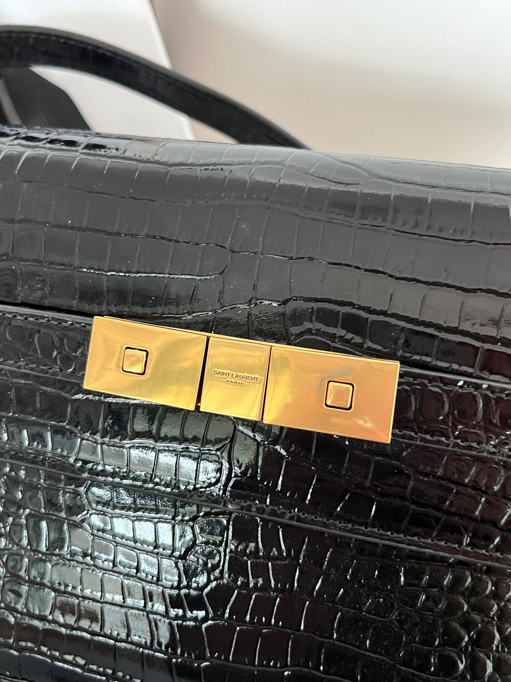Close-up of crocodile-embossed black handbag clasp with gold plate