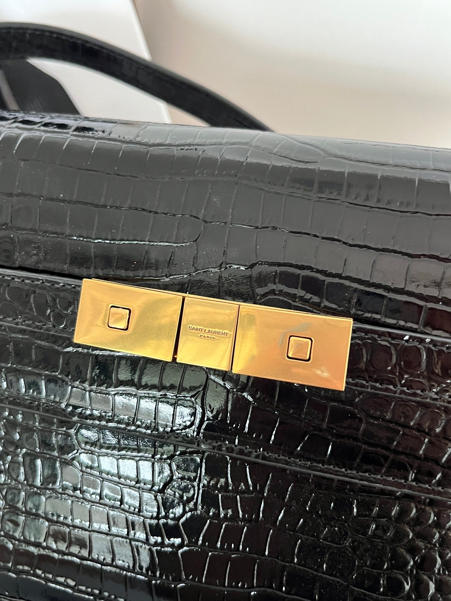 Close-up of crocodile-embossed black handbag clasp with gold plate