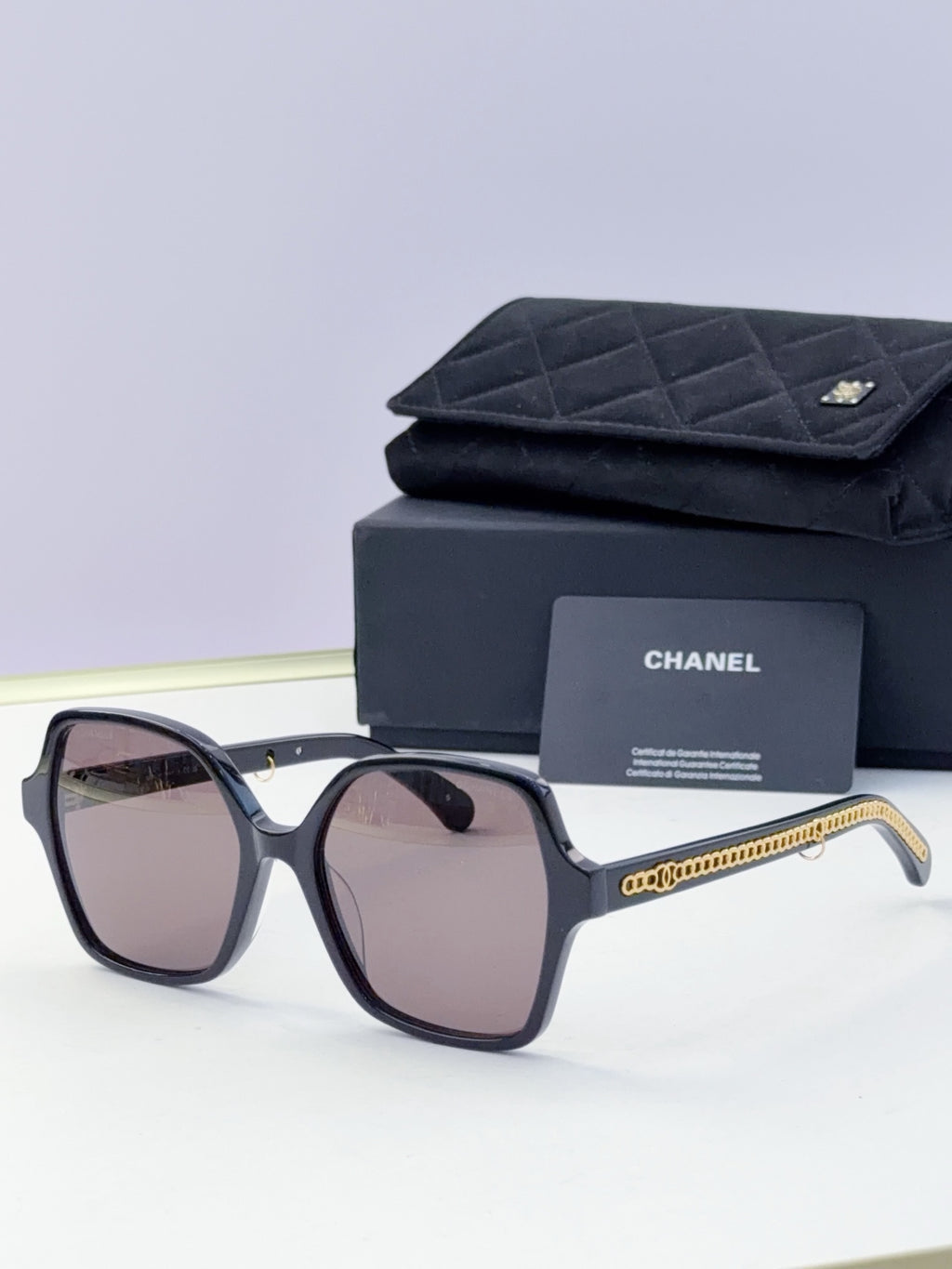 Eyeglasses with dark frame, pink-tinted lenses, gold chain temple, with case