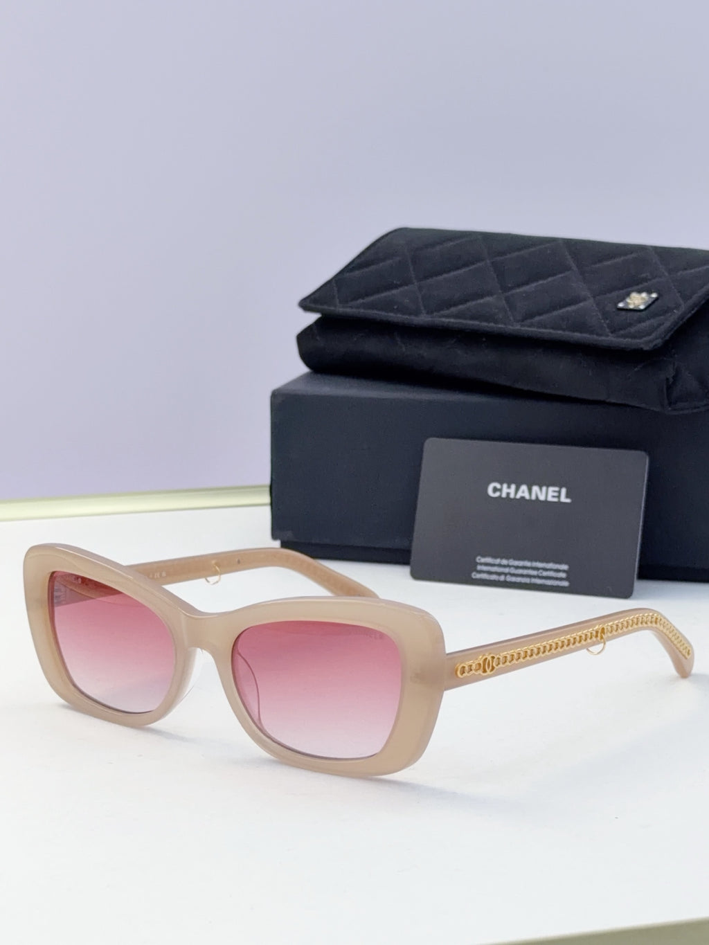 Light beige square sunglasses with pink lenses and gold chain temples