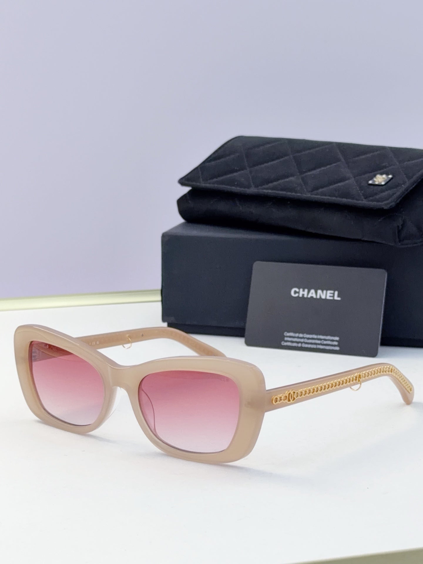 Light beige square sunglasses with pink lenses and gold chain temples