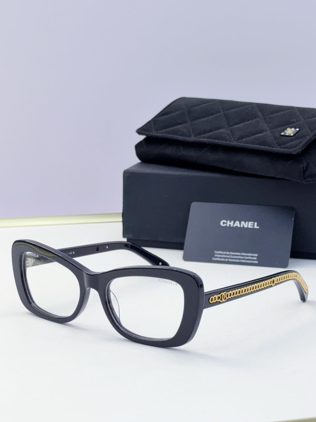 Black square sunglasses with clear lenses and gold chain detail on temples