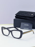Black square sunglasses with clear lenses and gold chain detail on temples