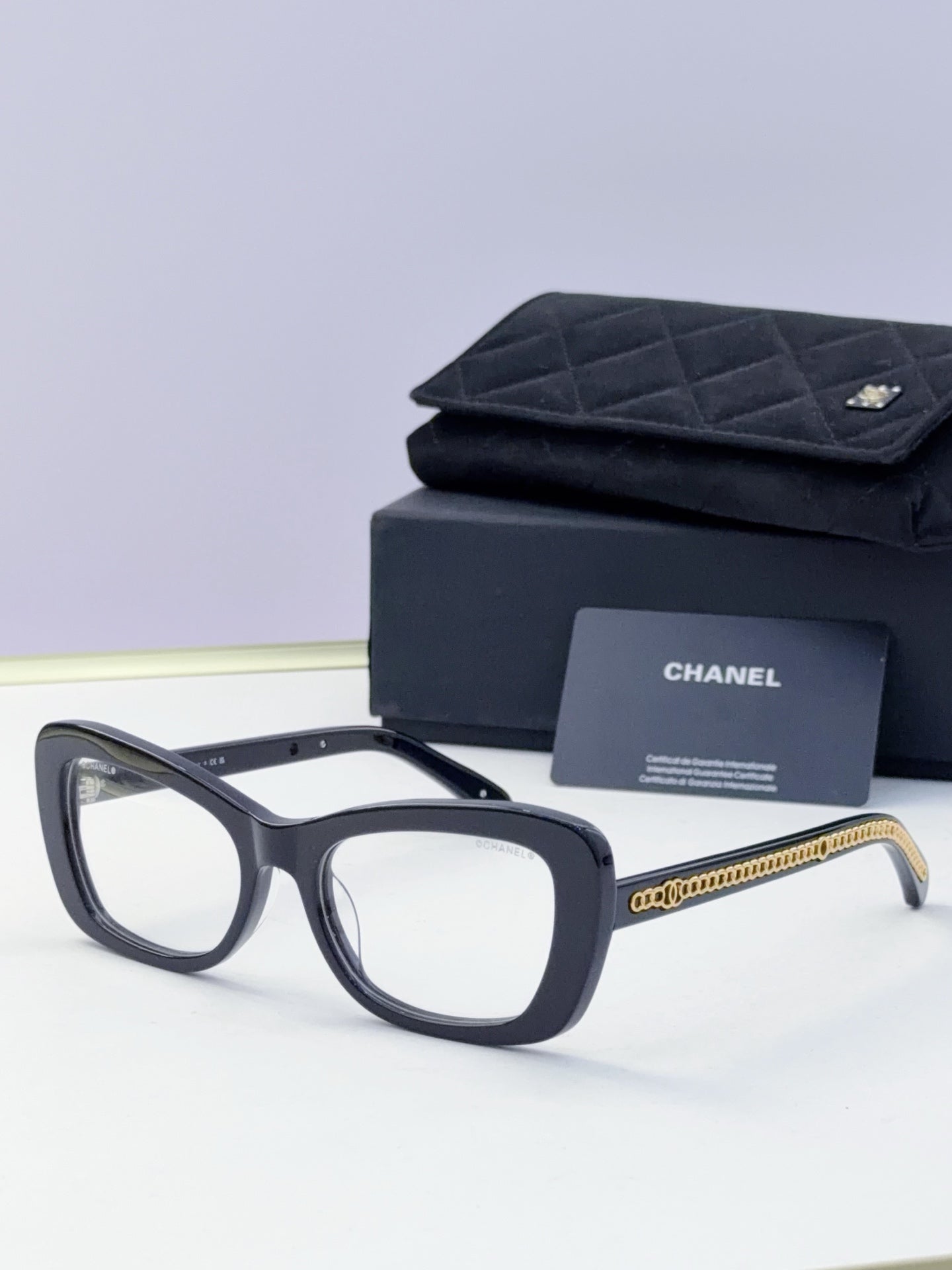 Black square sunglasses with clear lenses and gold chain detail on temples