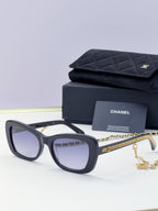 Black square sunglasses with tinted lenses and gold chain detail on temples