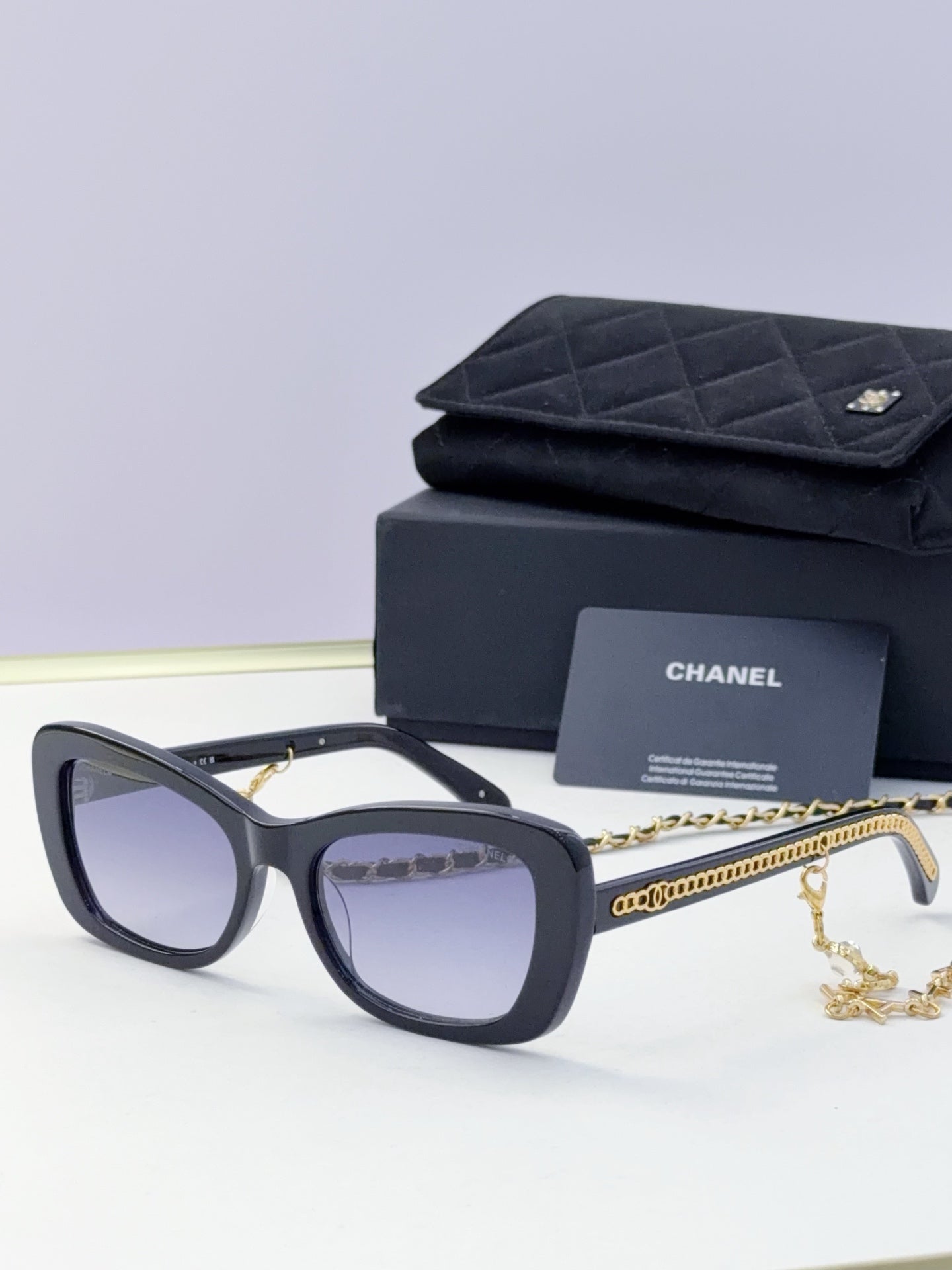 Black square sunglasses with tinted lenses and gold chain detail on temples