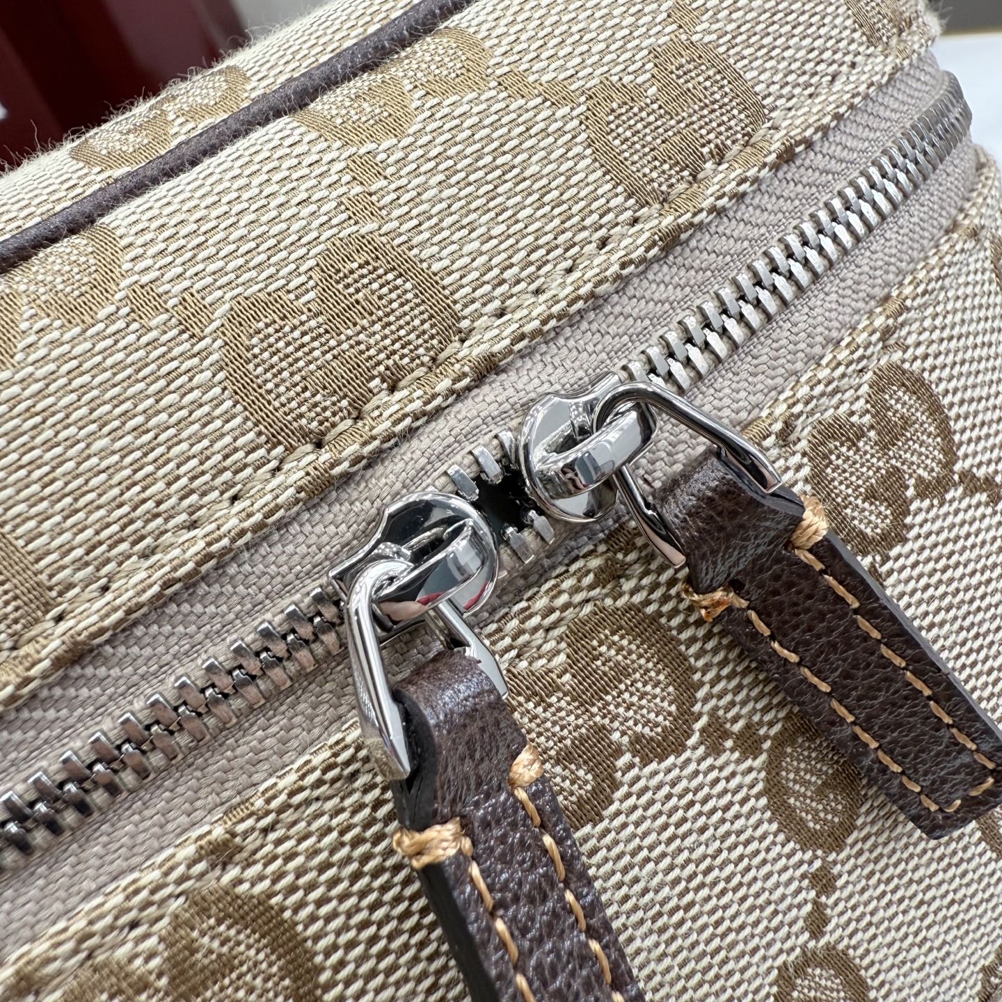 Handbag zipper close-up on beige GG canvas with silver zipper and dark leather tab