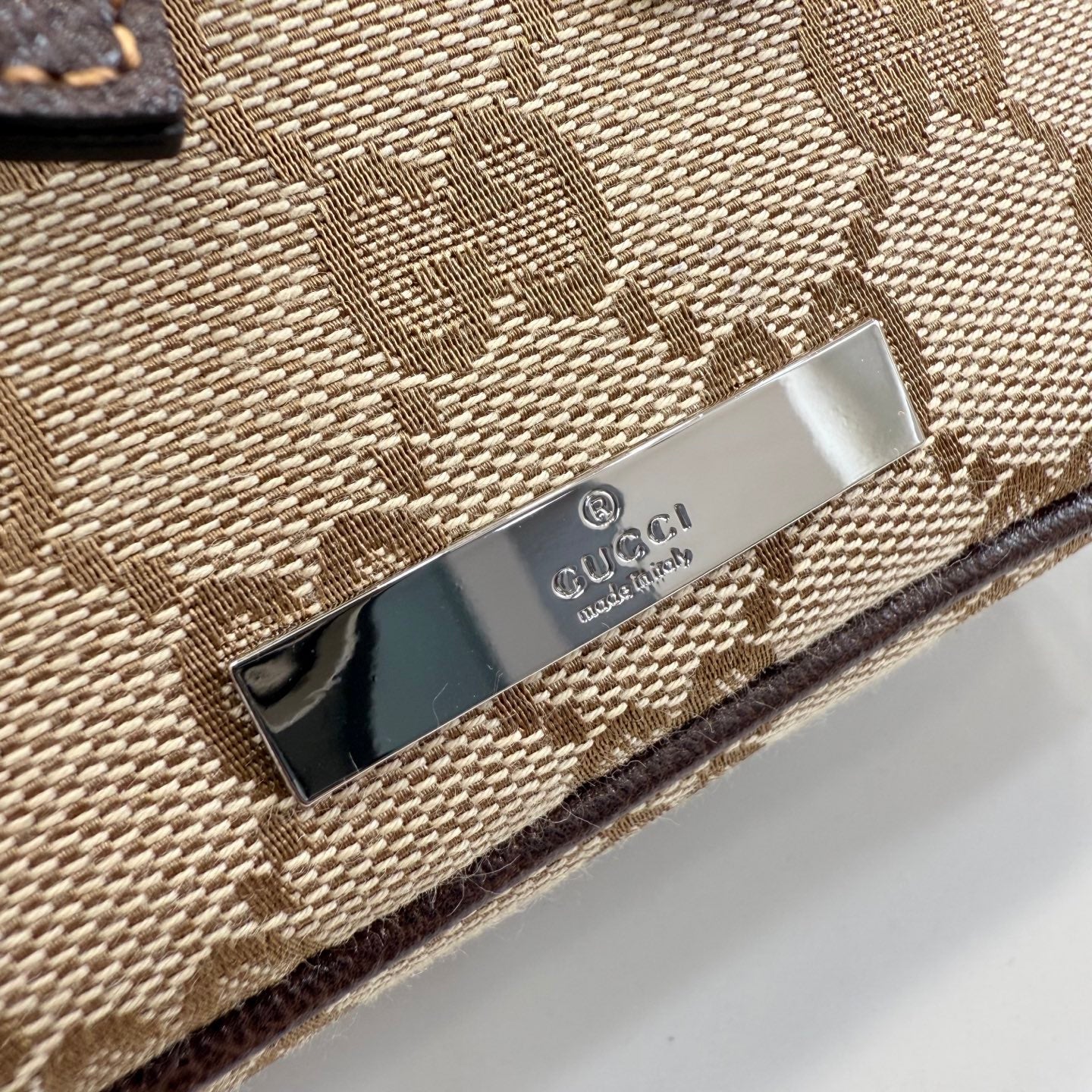 Handbag logo plate close-up on beige GG canvas with silver label and dark border