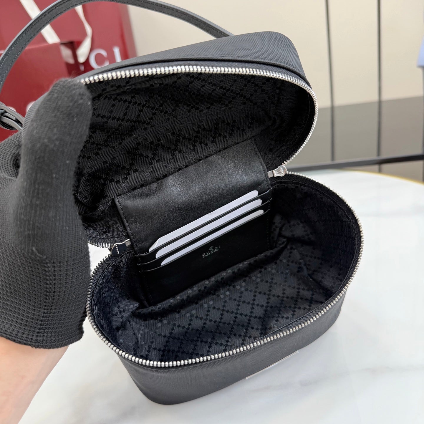 Opened black mini bag interior with patterned lining and zip pocket compartments